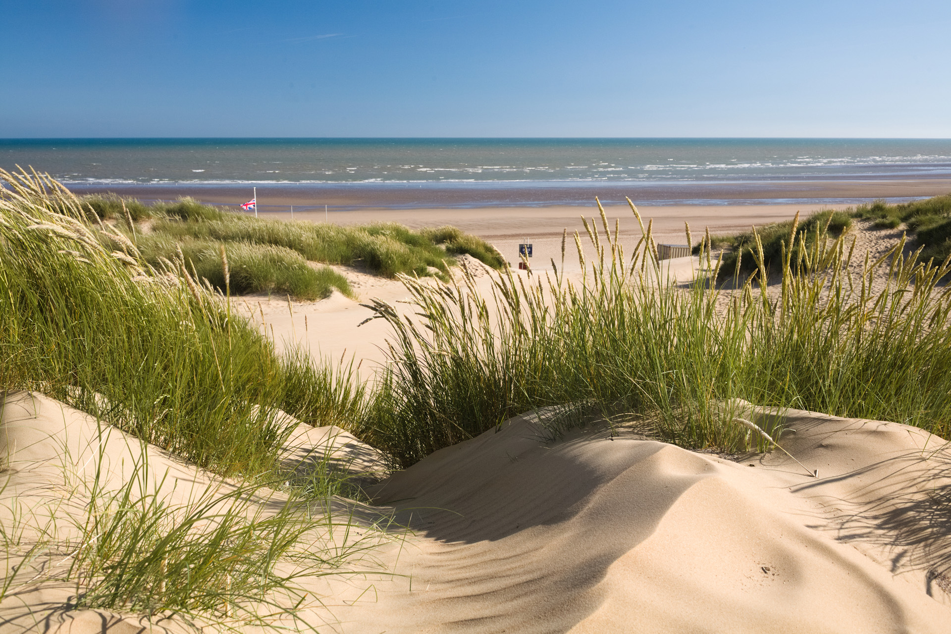 Creative photograph of sand dunes against a blue sky with broken cloud, taken at Camber Sands, England.