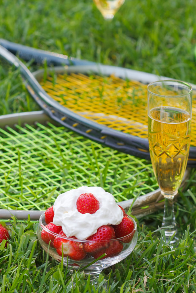 Strawberries with whipped cream, glass with champagne and tennis equipment on Wimbledon tournament grass. Wimbledon Grand slam celebration concept.