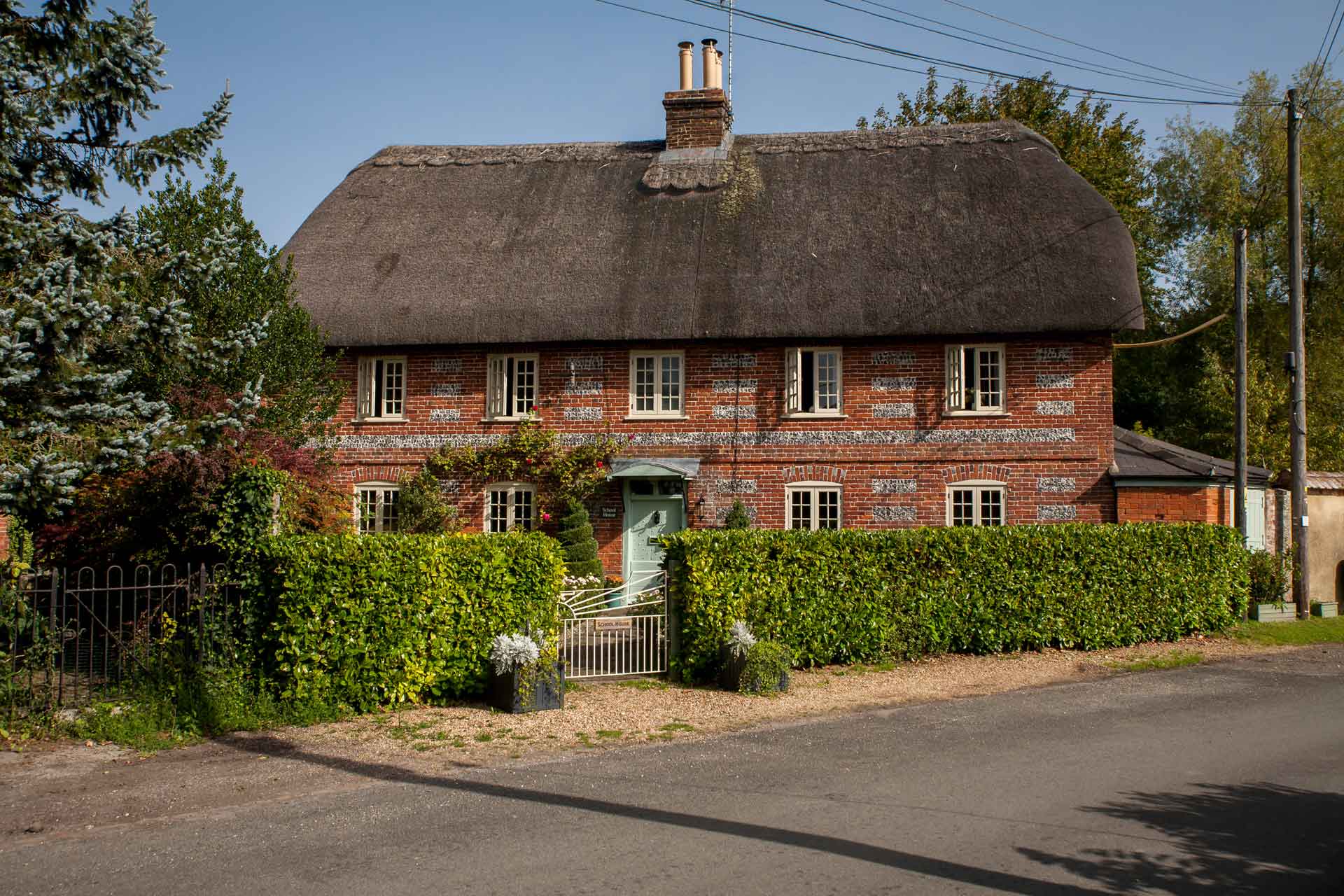 Red brick thatched cottage with box hedges and a driveway.