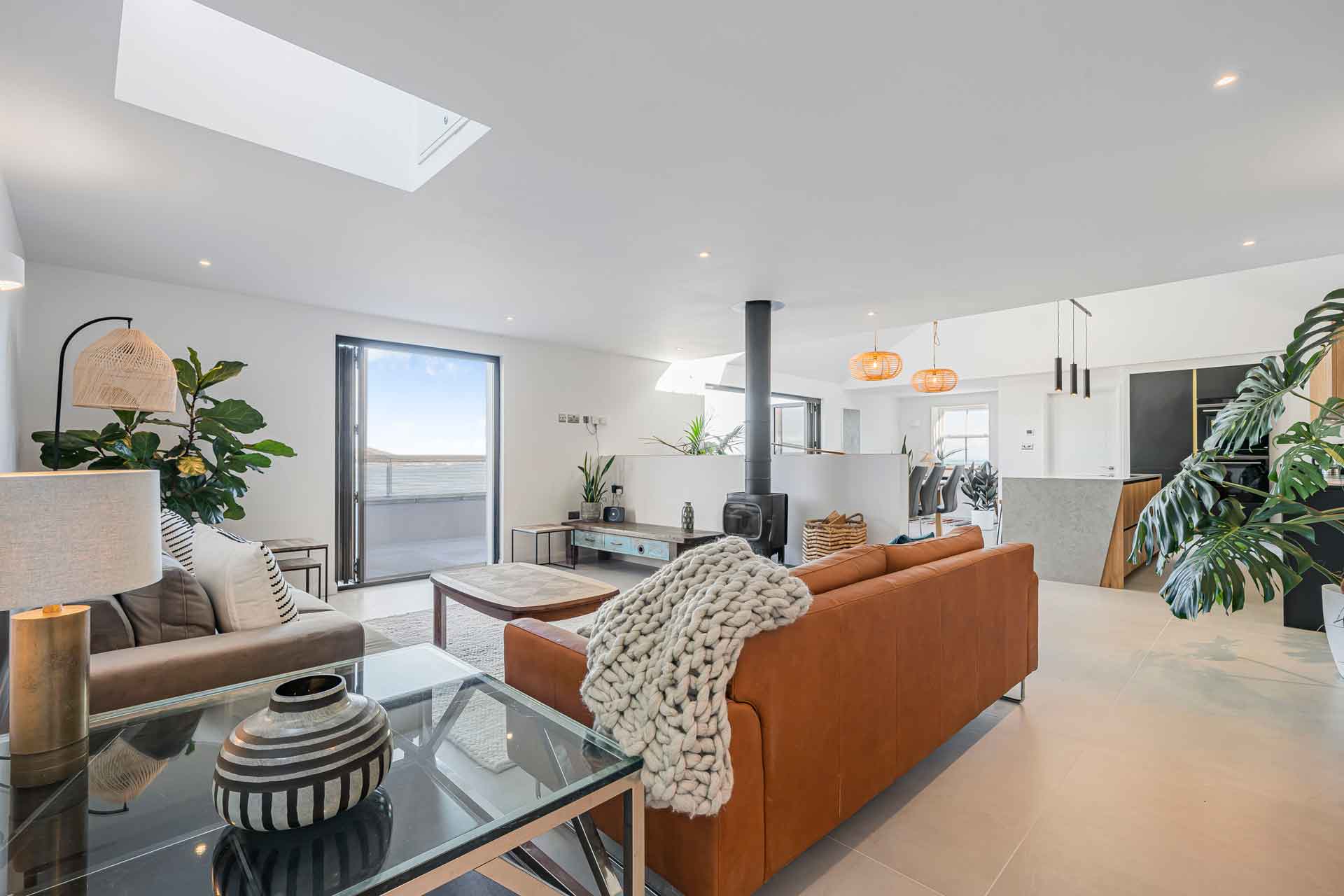 Living room with a burnt orange sofa, cream accents, a wood-burning stove and views of the Cornish coastline.