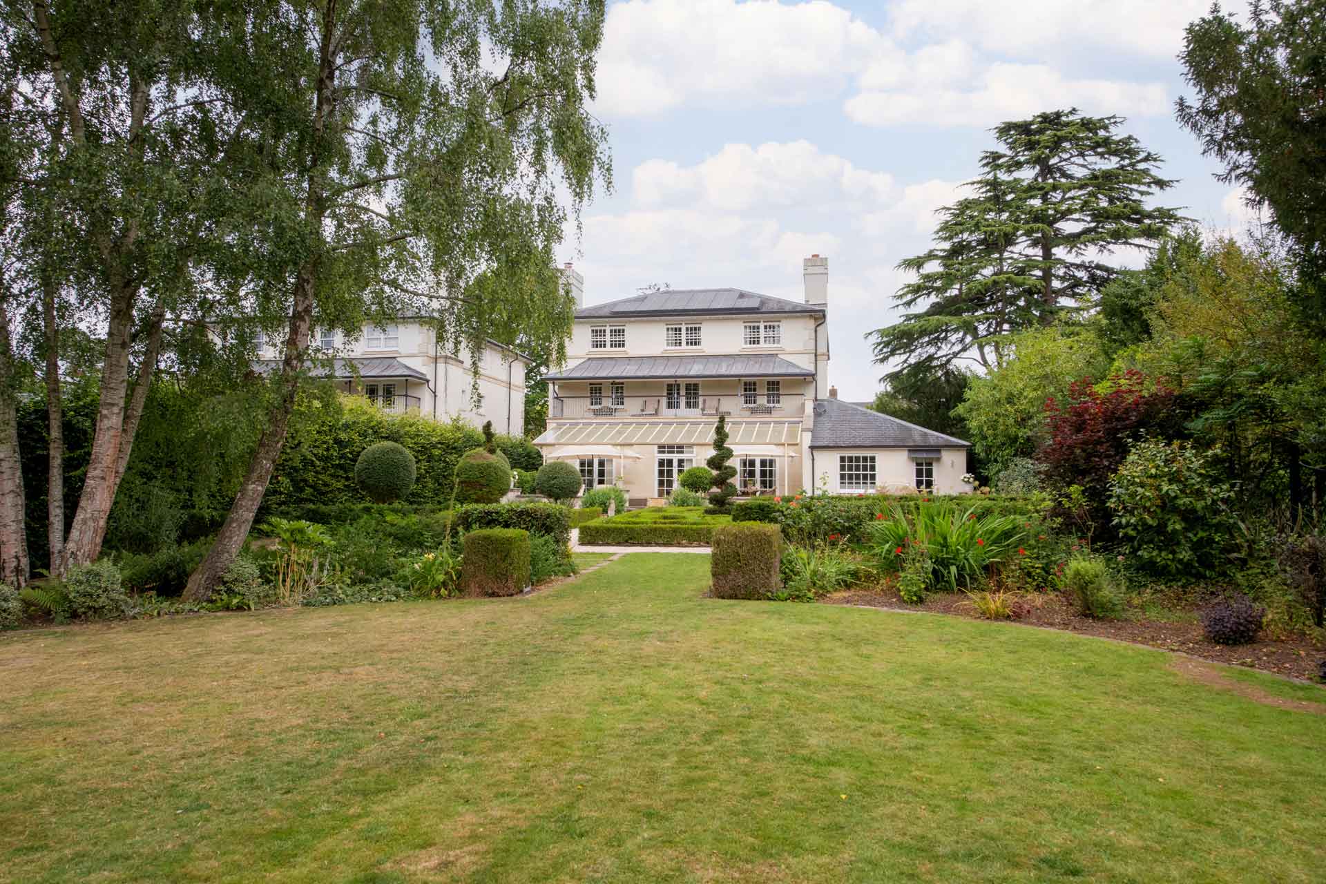 Exterior view of large neoclassical-style villa with terrace and large lawn.