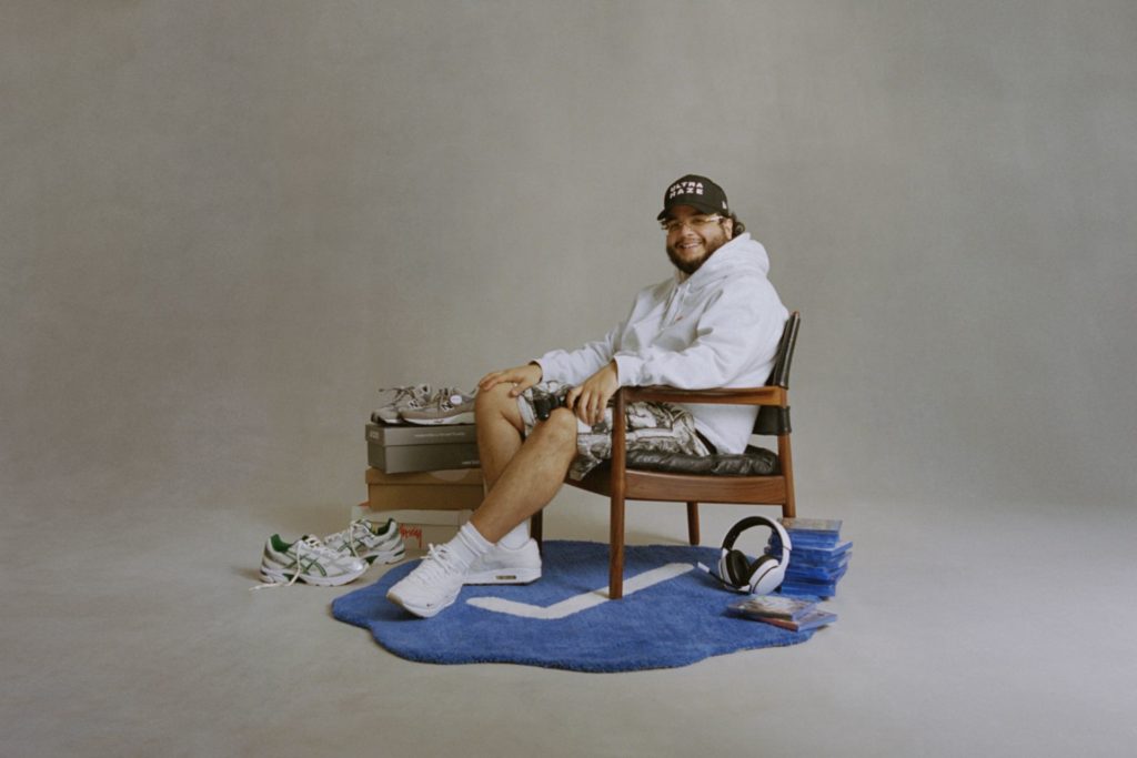 Alhan Gencay sitting in a wooden armchair surrounded by sneakers