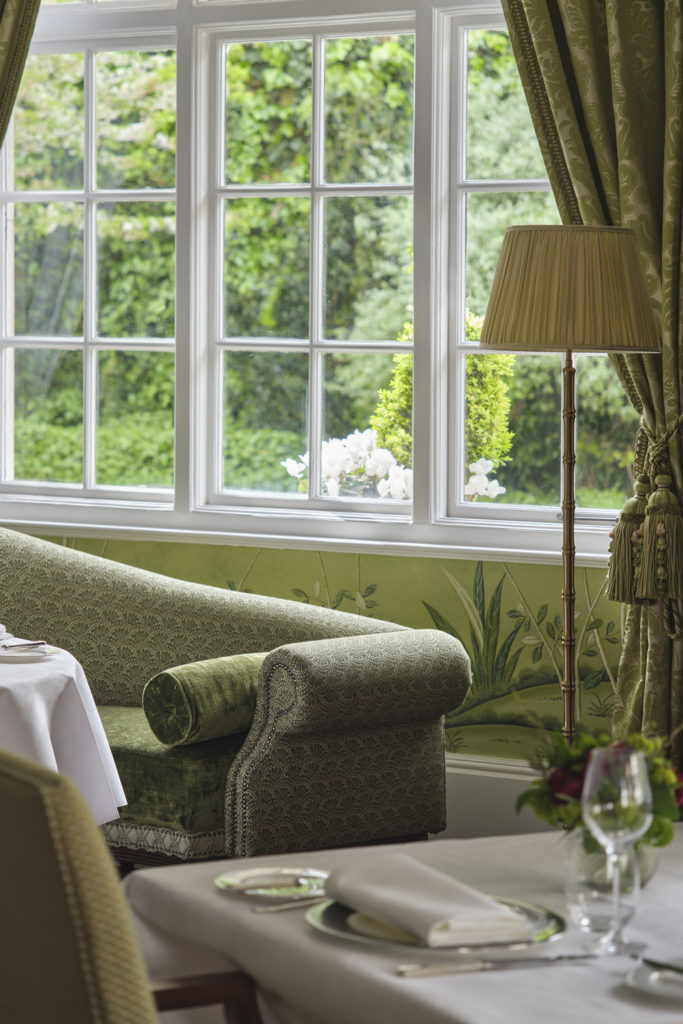 A green sofa beside a window at The Dining Room at The Goring