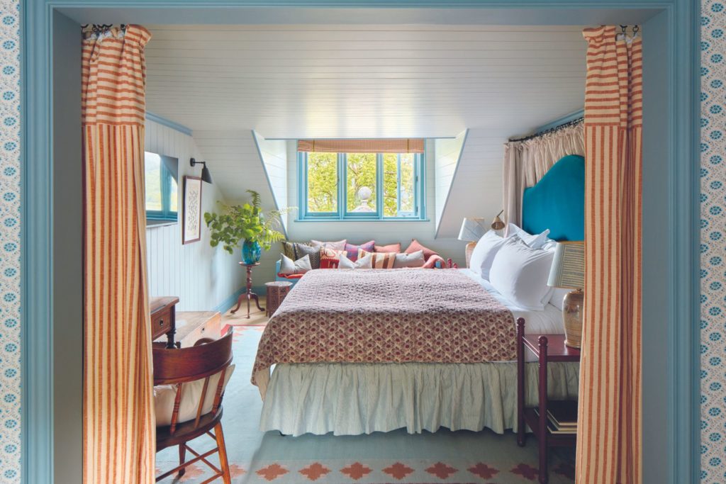 Hotel bedroom with pale blue walls, a patterned pink bedspread and orange curtains.