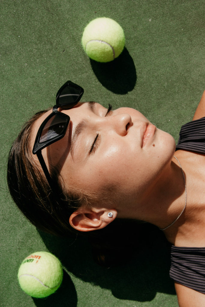 Woman lying down with tennis balls around her | wimbledon pre-loved fashion