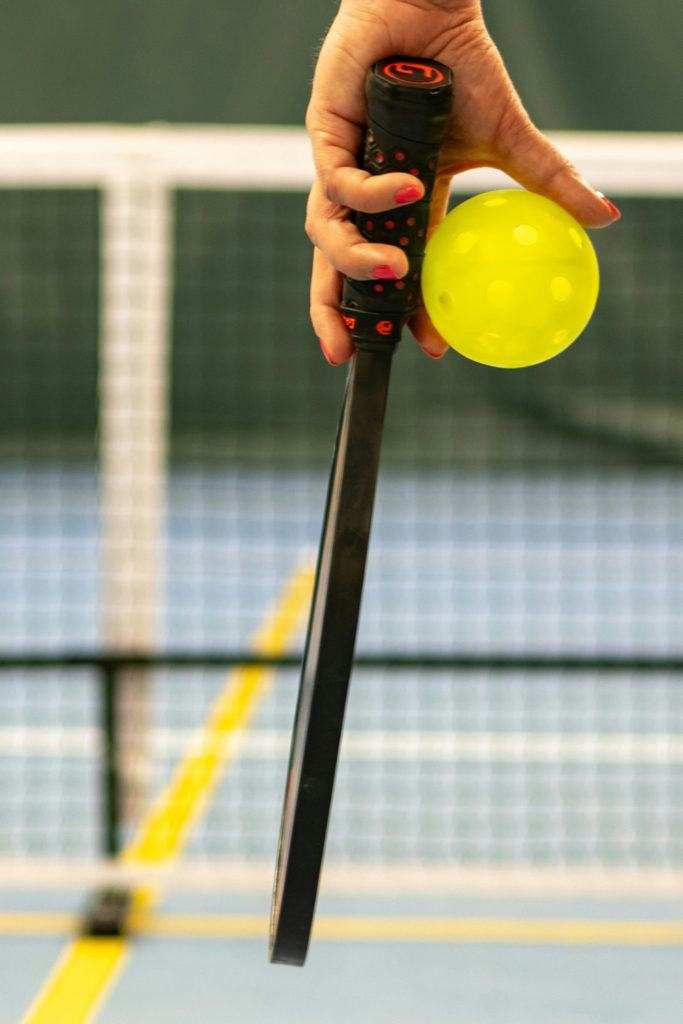 A hand holding a Pickleball racket and ball