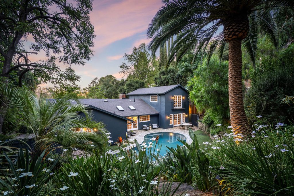 Woodlands home at dusk, with a swimming pool and palm trees.