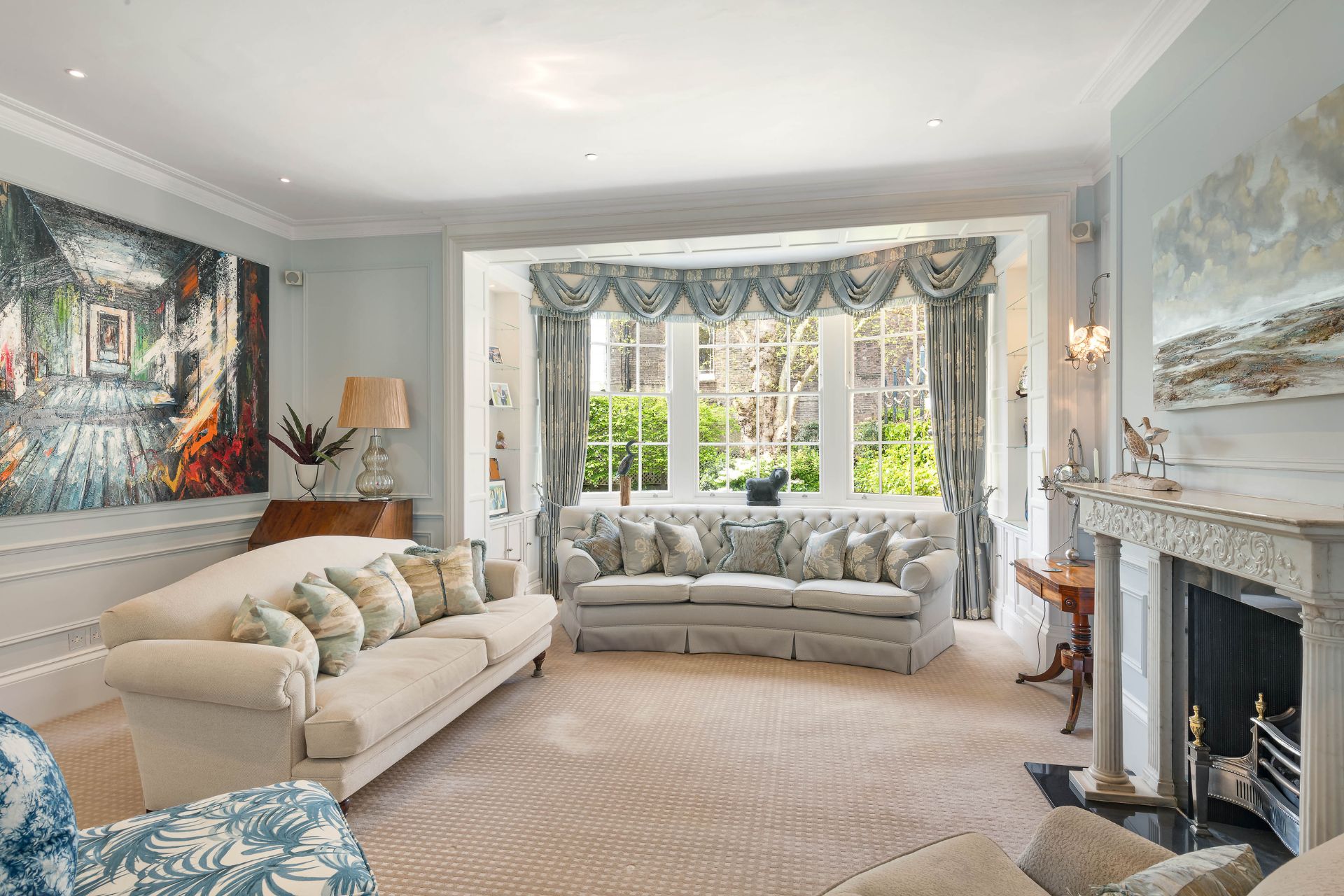 Living room with bay window, cream sofas and pale blue walls.