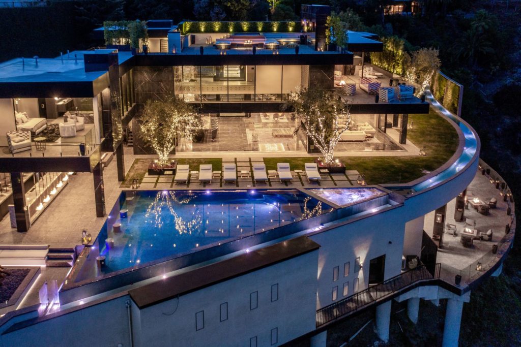 Aerial view of LA mansion with infinity pool, hilltop balcony and floor-to-ceiling windows.