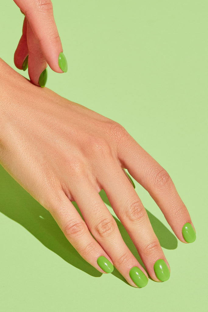 Hand with neon green manicure on green background