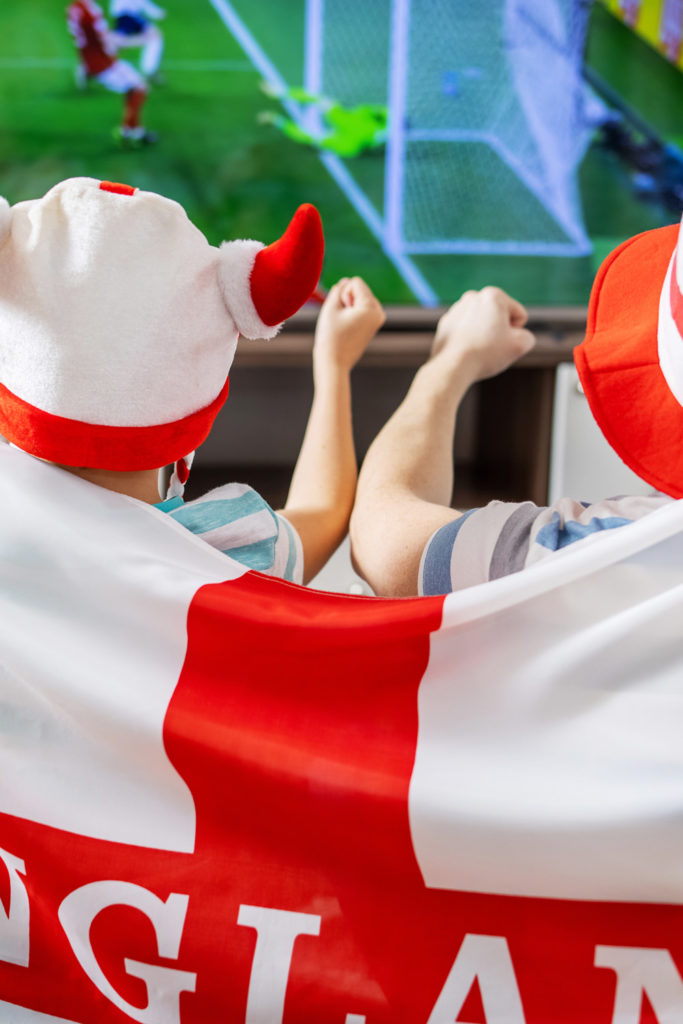 Father and son with England flag watching football game on TV and supporting their national football team