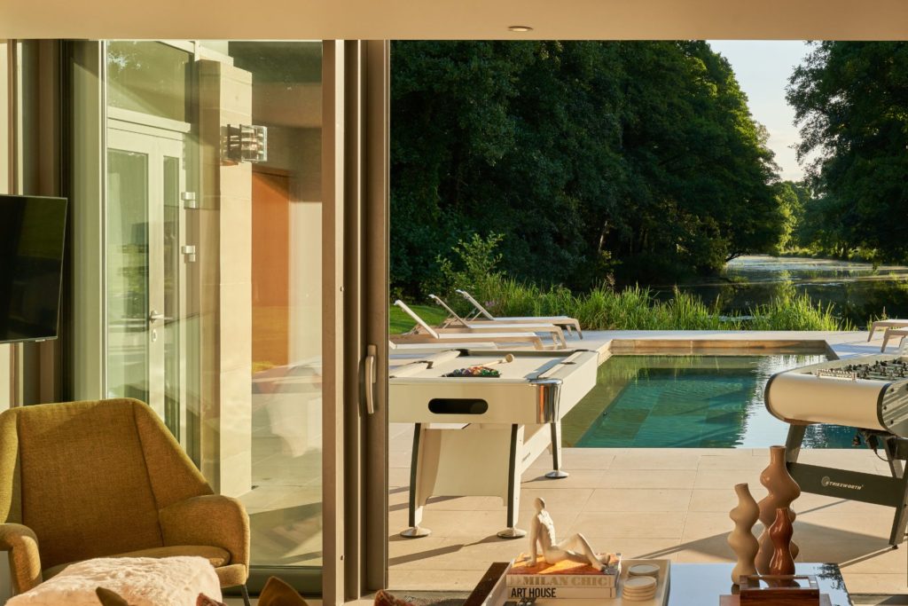 Games room with armchair, table football and bi-fold doors opening onto an outdoor pool area