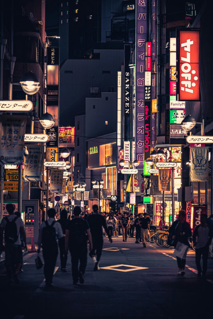 People Walking on the Street Between Buildings at night in Tokyo, Japan