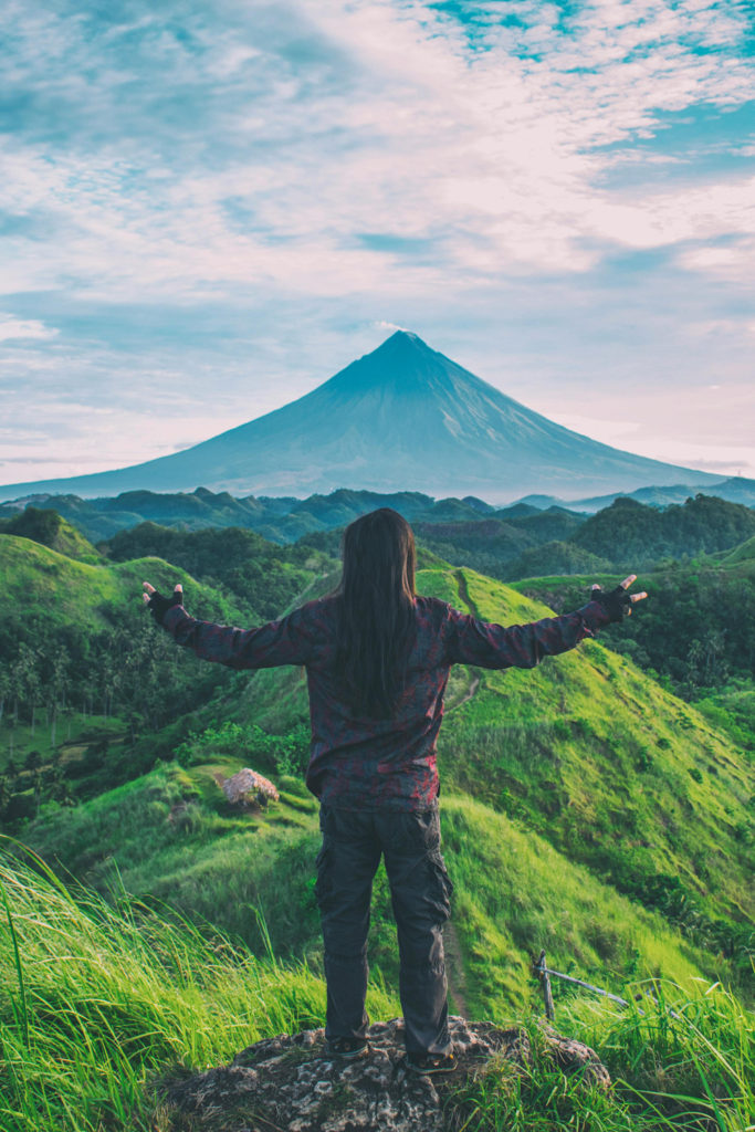 A person standing in front of a green scene with a mountain in the background