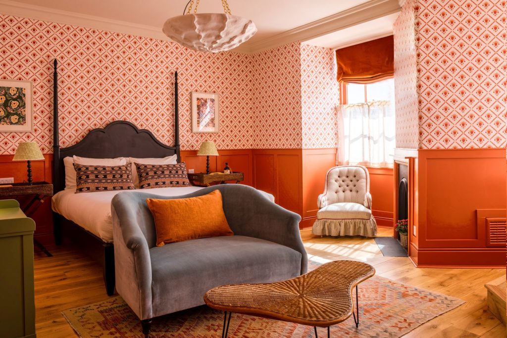 Hotel bedroom with coral patterned wallpaper, a grey velvet sofa and coral panelling