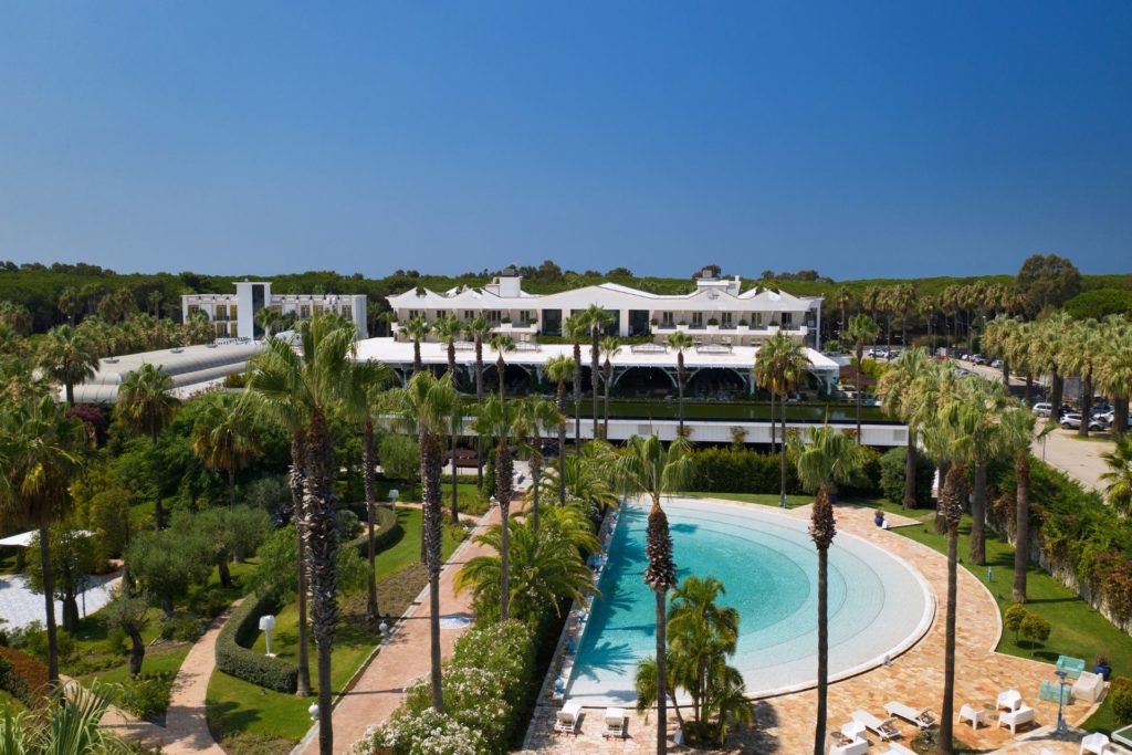 Aerial view of Savoy Beach Hotel & Spa, with a semi-circular pool and palm trees