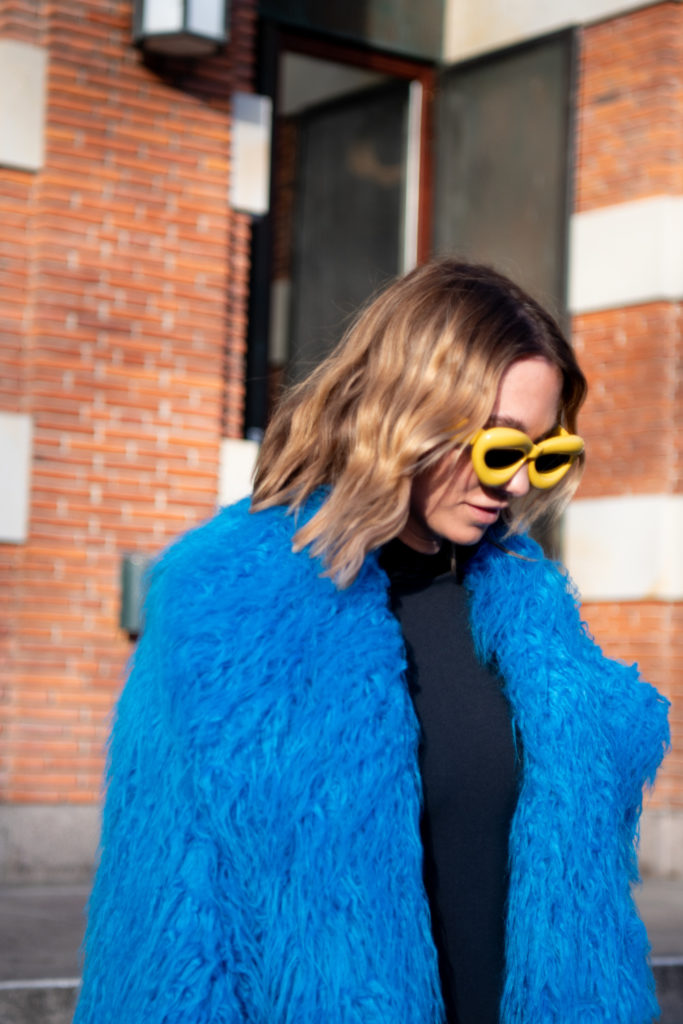 Qoman with textured bob wearing yellow sunglasses and blue fluffy coat