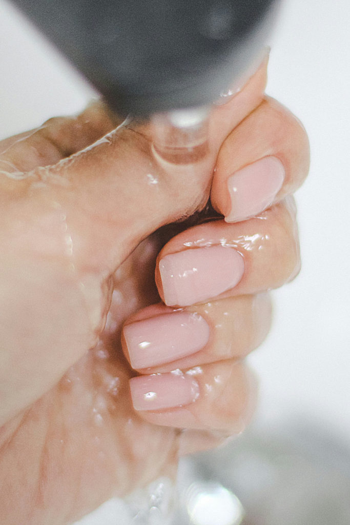 Hand with bubble bath nails under running tap