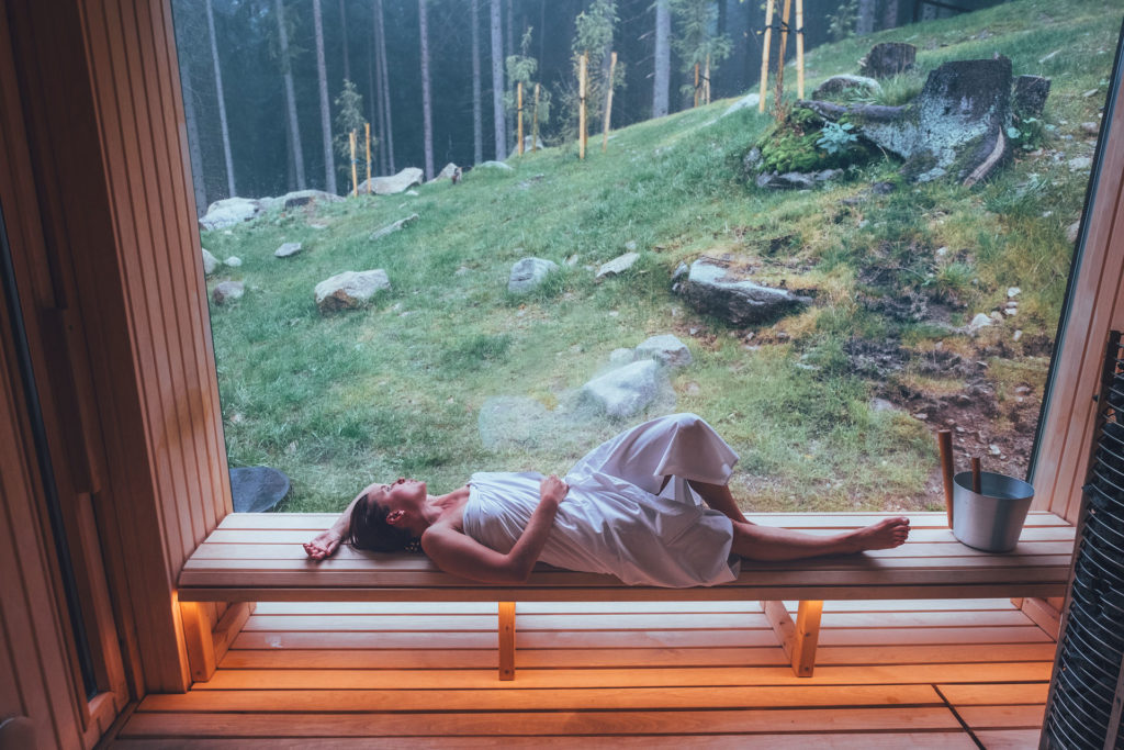 Woman lying in an outdoor sauna by the forest | wellness trends 2025