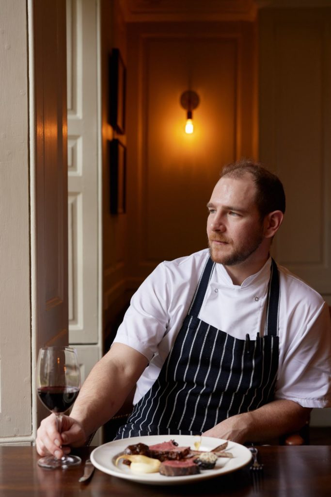 Chef Jake Simpson ith a glass of red wine and a roast dinner