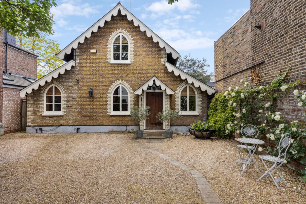 Coachh ouse with arched windows and flowers in the driveway