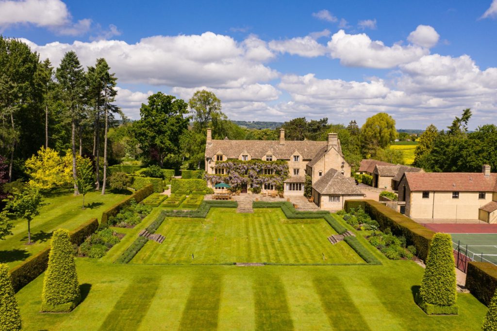 Aerial view of wisteria-clad Cotswolds home with landscaped lawns.