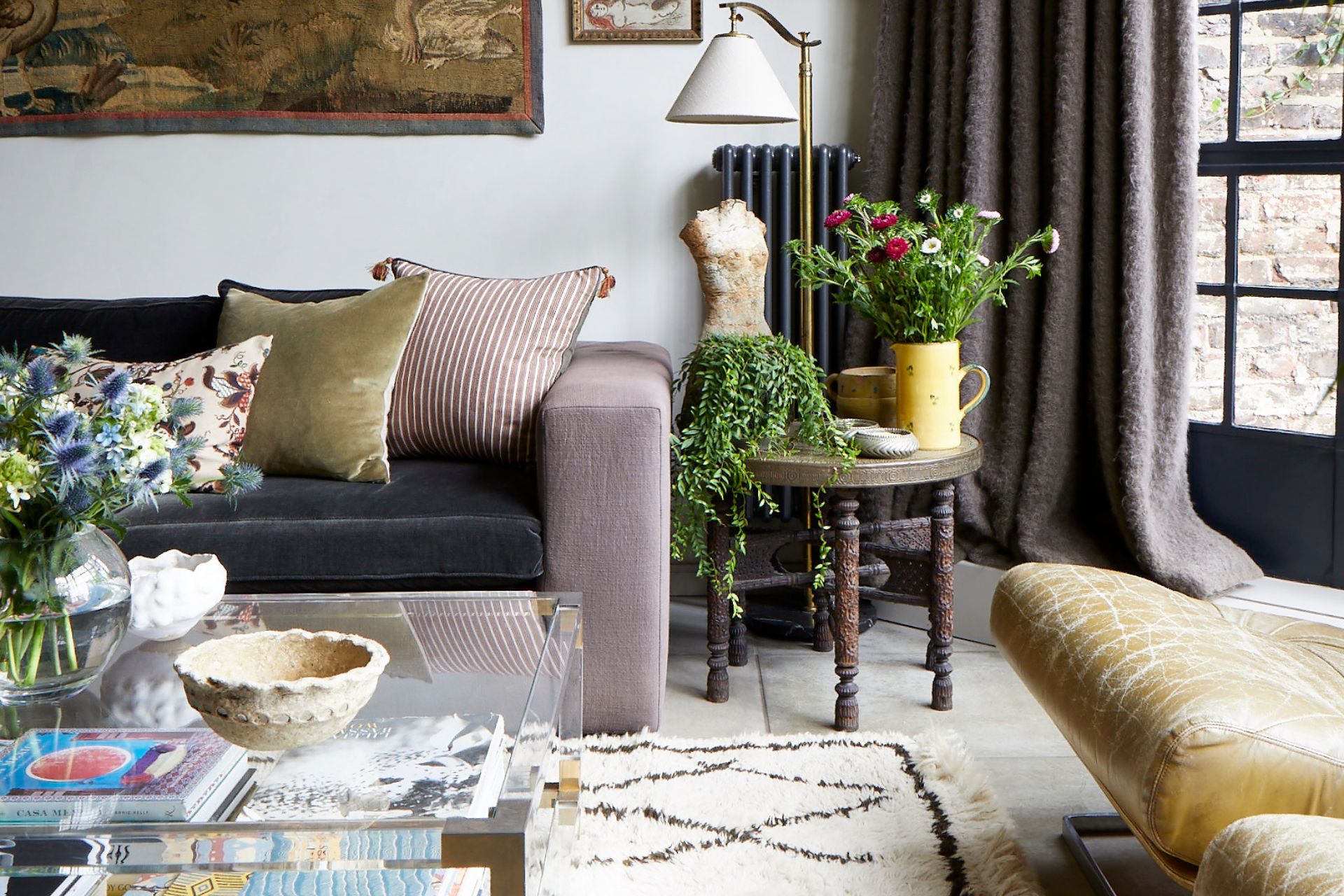 Pale pink sofa, mustard yellow velvet cushions, white rug and glass coffee table with houseplants