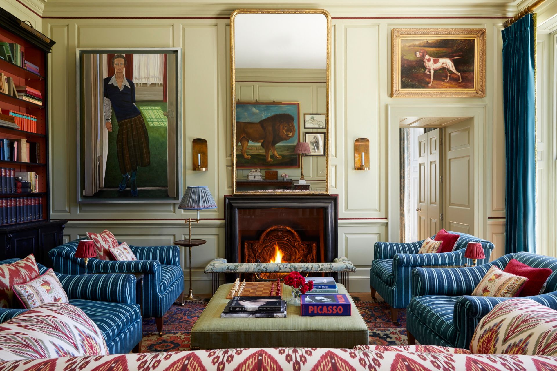 Large living room with blue stripe armchairs, a red patterned sofa, a period fireplace and a large gilded mirror