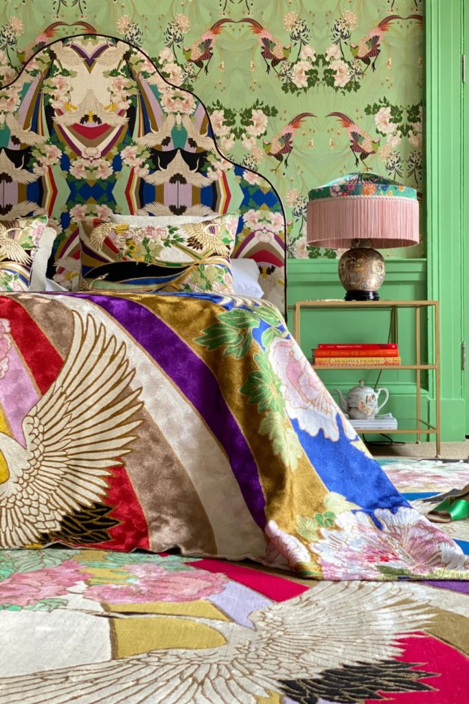 Light green walls with a floral tapestry and a bed with a colourful bedspread